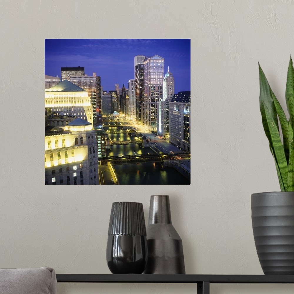 A modern room featuring Large, square photograph of the Chicago River surrounded by lit skyscrapers on three sides, at ni...