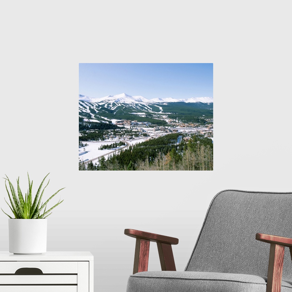 A modern room featuring Photograph of aerial view of city that is covered in snow with mountains in the distance and fore...