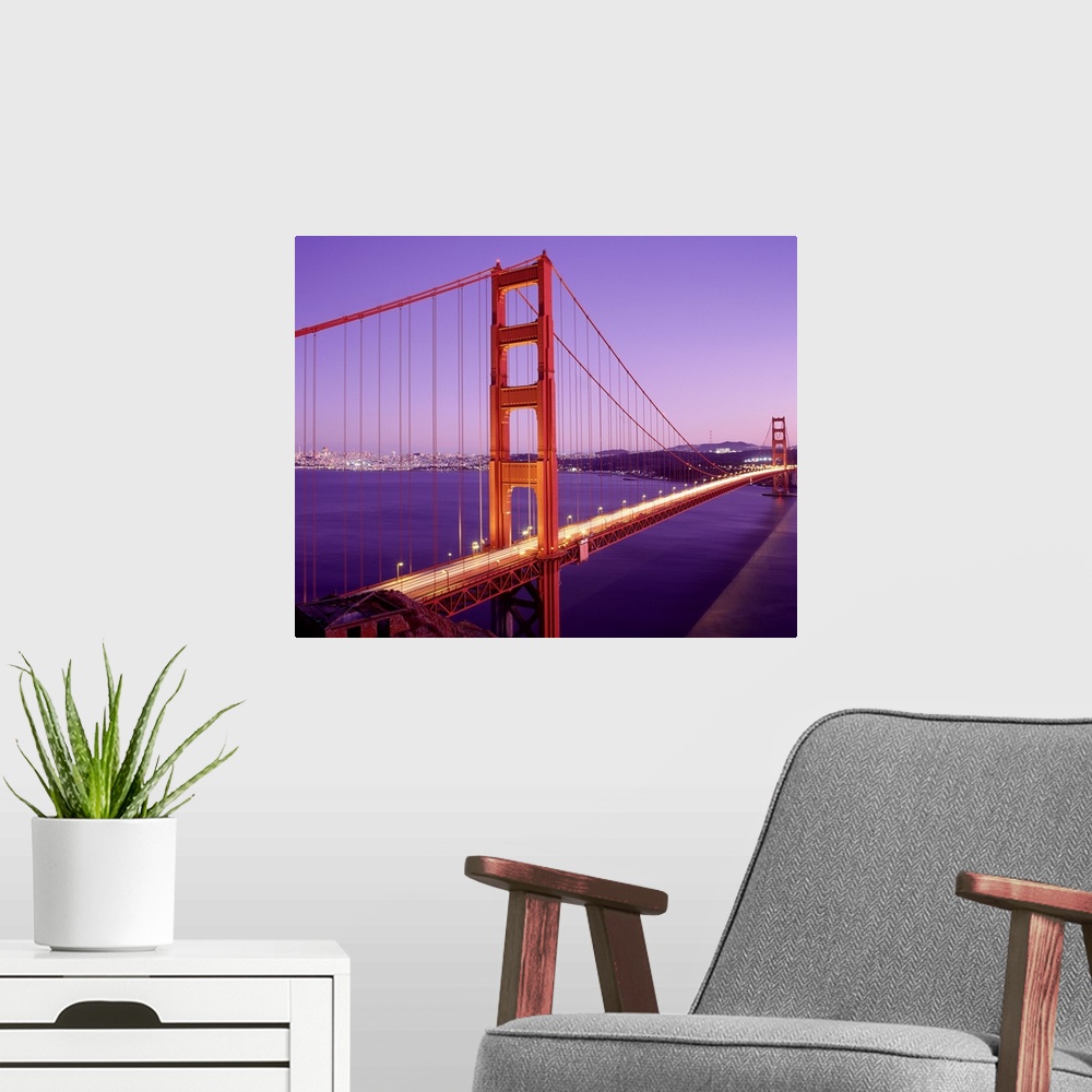 A modern room featuring Cars driver over the Golden Gate Bridge in San Francisco as the setting sun creates purple hues i...