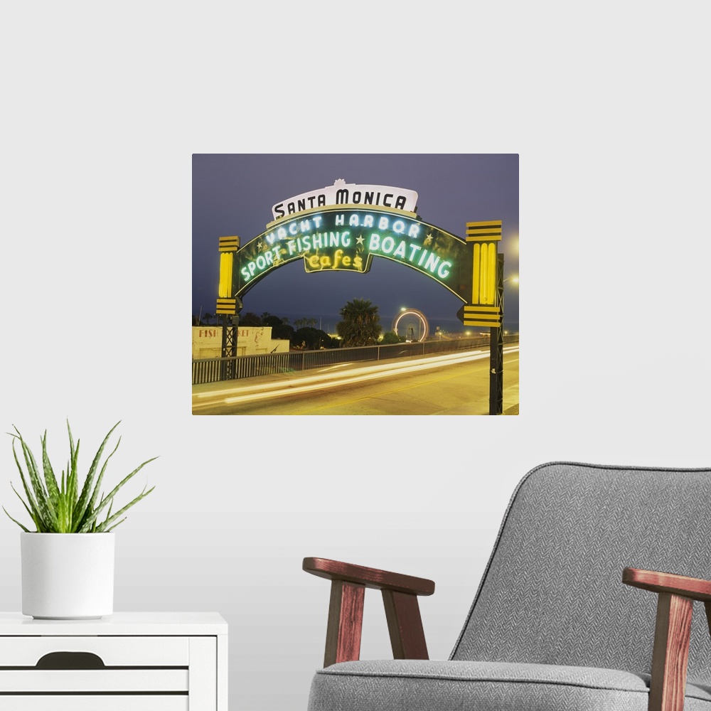 A modern room featuring Long exposure shot of a lit up Santa Monica Pier sign at night as traffic headlights go by and th...