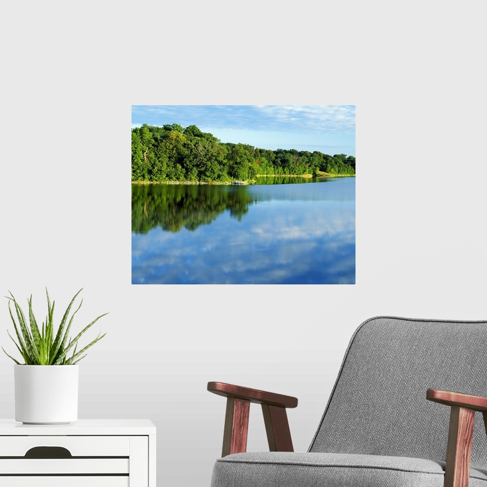 A modern room featuring Thick forest curves and lines a large body of water while reflecting in it.