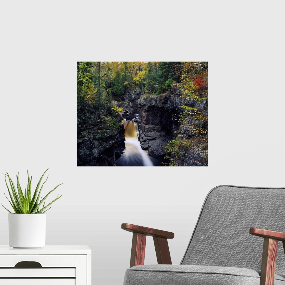 A modern room featuring Landscape photograph of a fall colored forest on top of tall rocky cliffs that rise above a water...