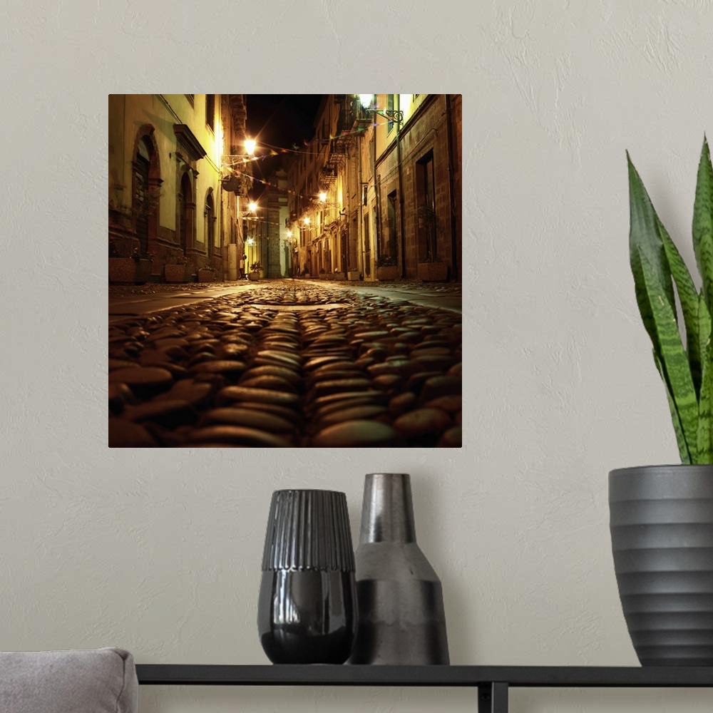 A modern room featuring Cobblestone road in the city of Bosa, Italy, at night.