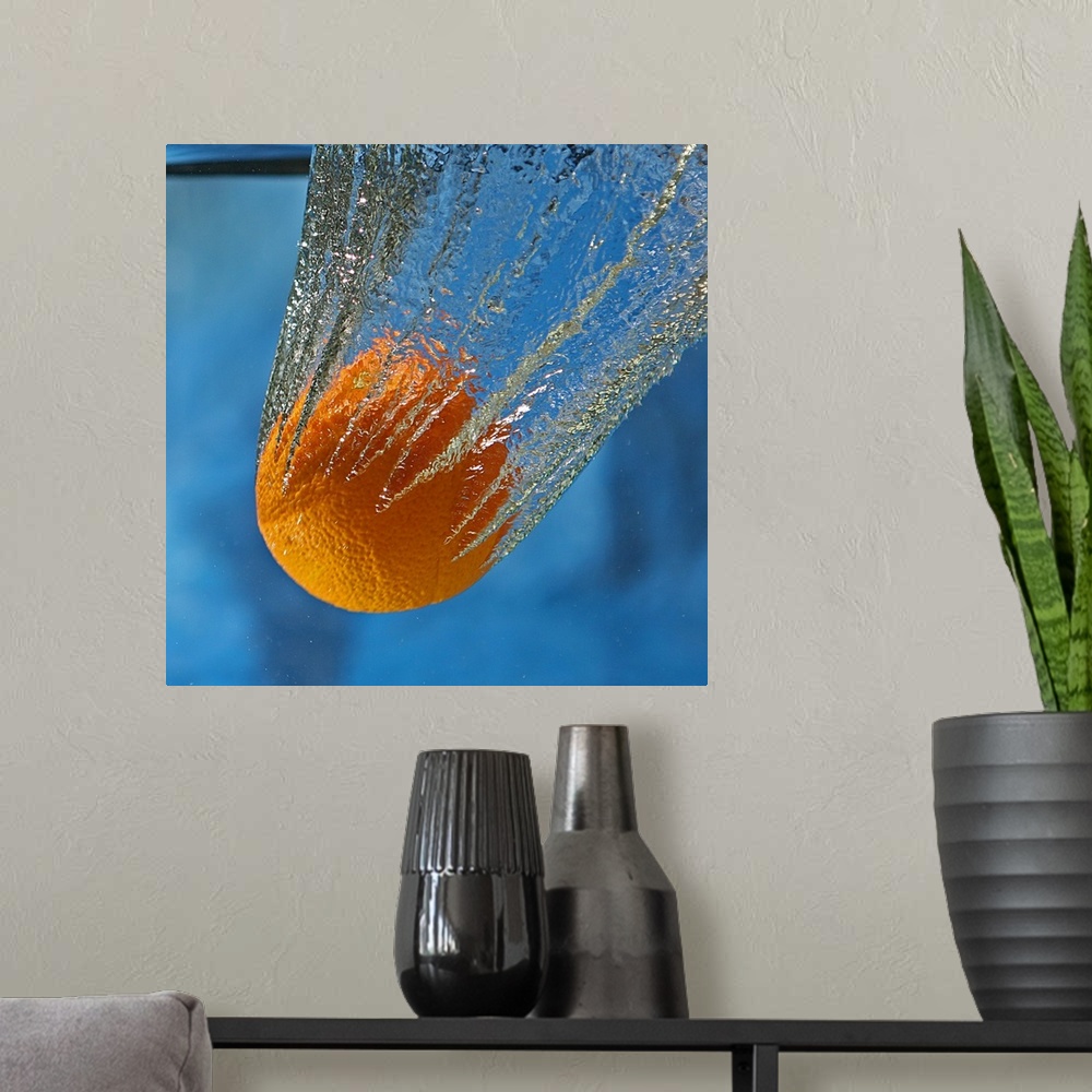 A modern room featuring An orange splashing into a tank of clear water.