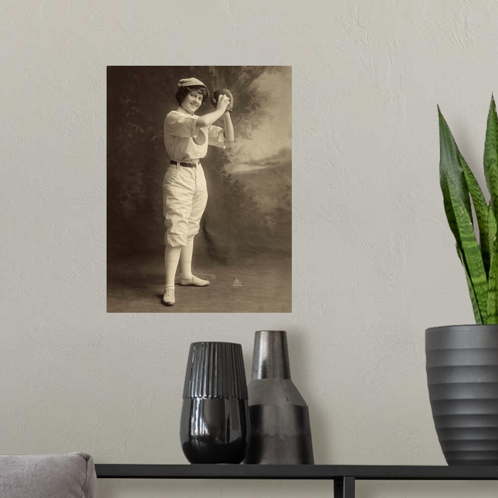 A modern room featuring A female baseball player, in uniform, in a pitcher stance. Photograph, 1913.