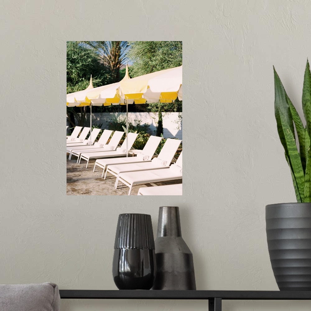 A modern room featuring Photograph of a neat row of pool loungers with rolled towels underneath yellow umbrellas.