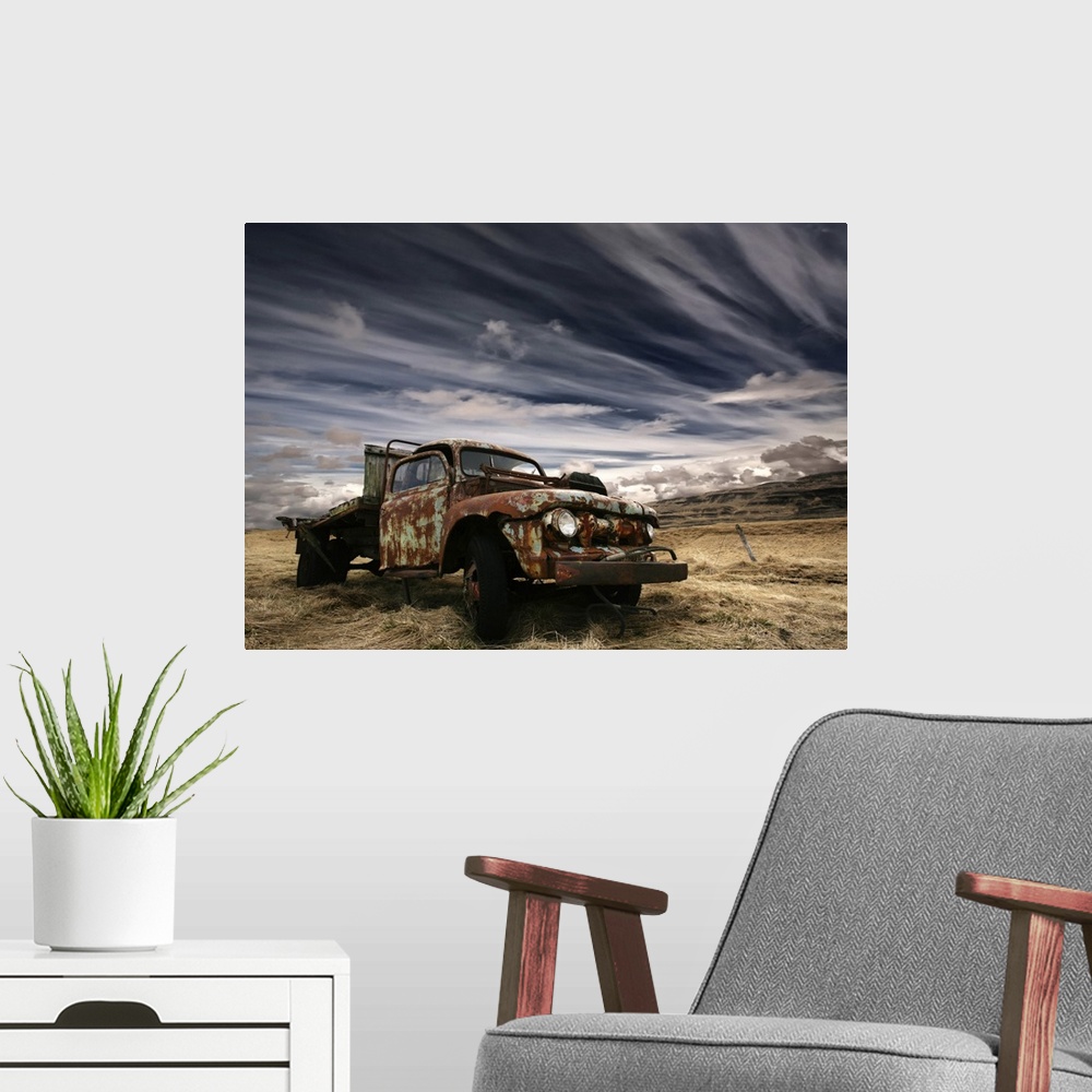 A modern room featuring An old rusted truck sits unused in a field under a sky with dramatic clouds.