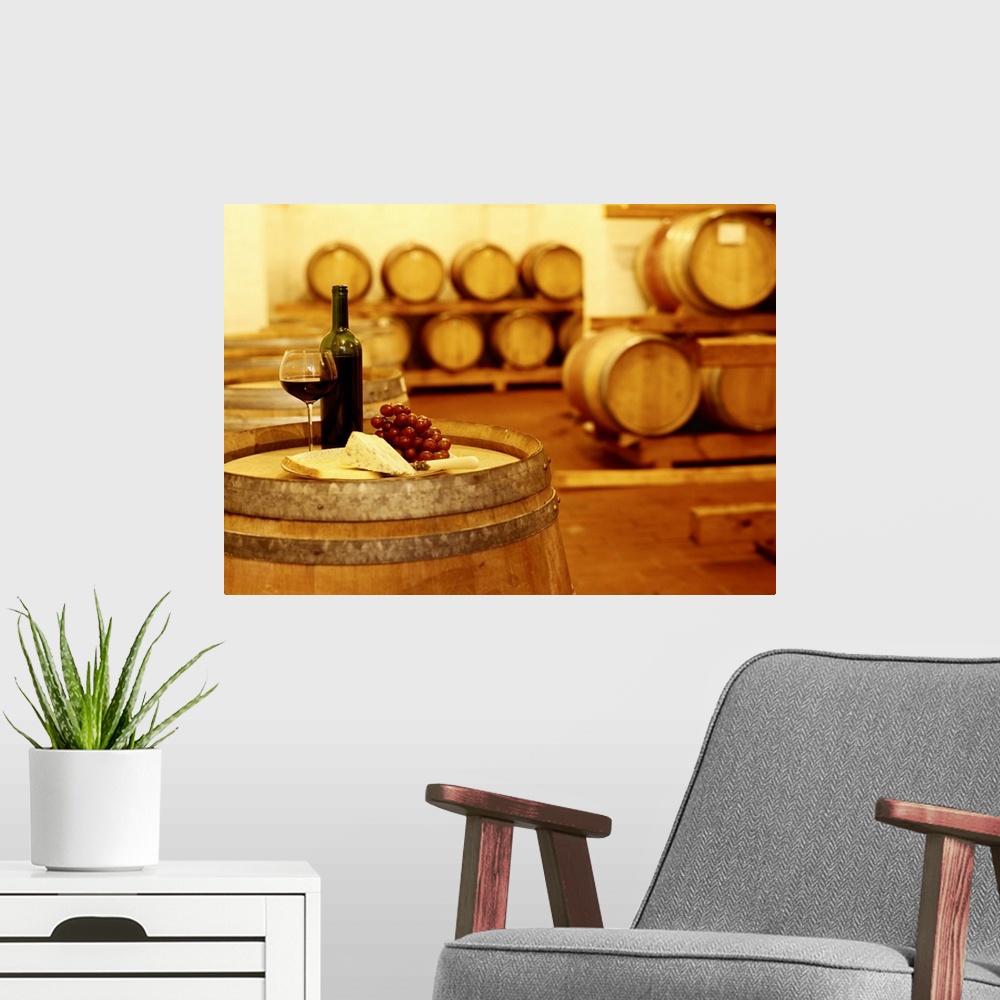 A modern room featuring A photograph in a wine cellar of an upright barrel with a glass of wine, grapes, and cheese sitti...