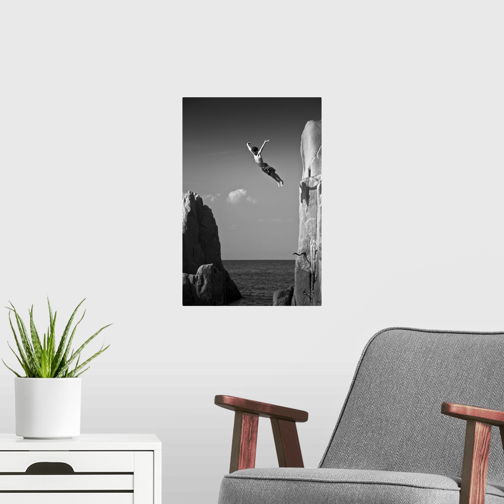 A modern room featuring A young man leaping off a cliff into the ocean, Sardinia, Italy.