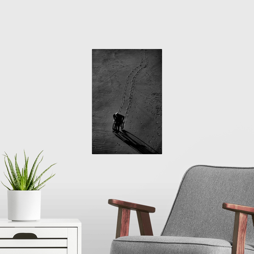 A modern room featuring Black and white photograph of a person using their wheel chair in the sand, leaving a lined trail...