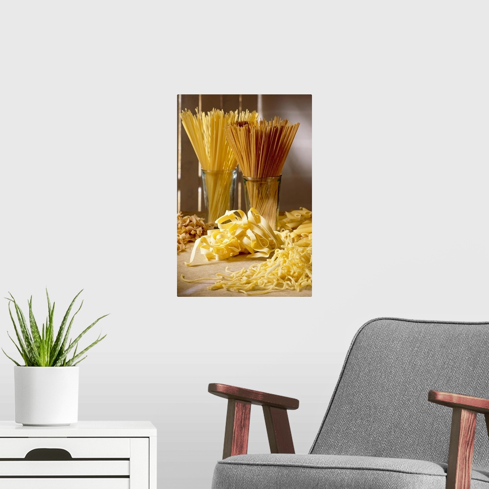A modern room featuring Dry pasta in glass jars and fresh pasta scattered in front of it is photographed artistically.