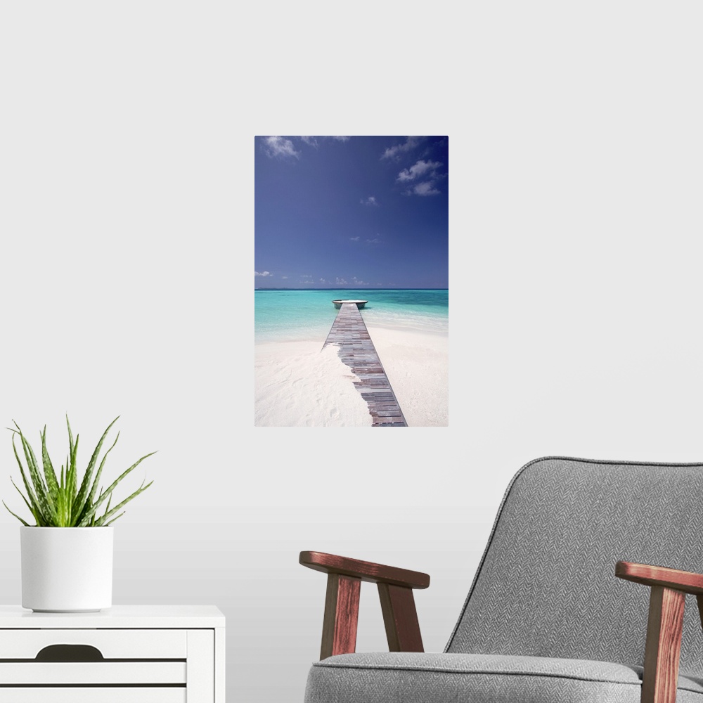 A modern room featuring Vertical photo of a wooden walkway stretching out into the tropical sea, partly covered in sand.