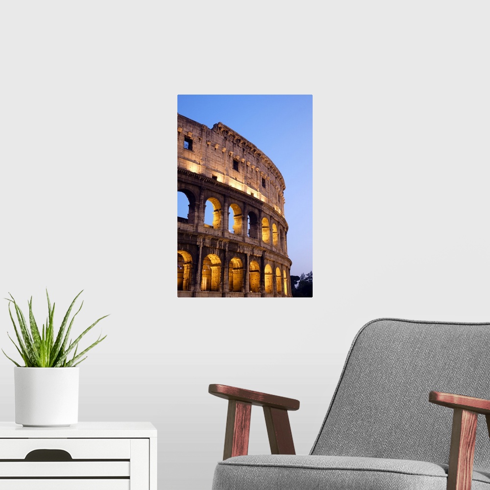 A modern room featuring Veridical photograph of the Roman Coliseum at dusk with the lights illuminating the arched windows.