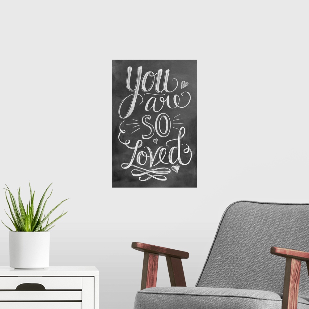 A modern room featuring The phrase "You are so loved" done in flowing hand-lettering in white chalk on a dark background.