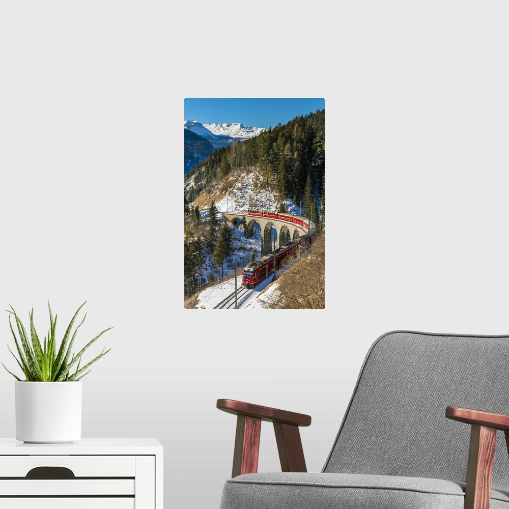 A modern room featuring The famous red train of Albula mountain railway passing through a scenic winter alpine landscape ...