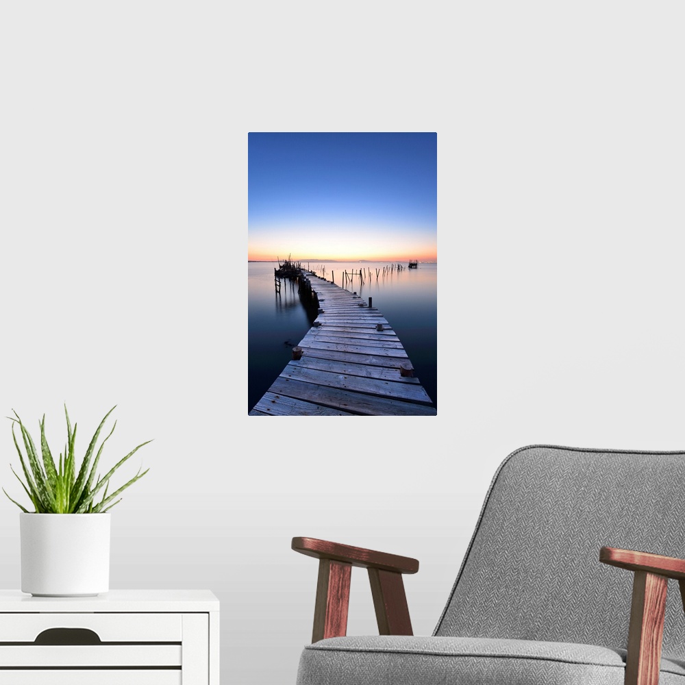 A modern room featuring Wooden pillars piers, a palafite fishing harbour of Carrasqueira at dusk. Alentejo, Portugal.