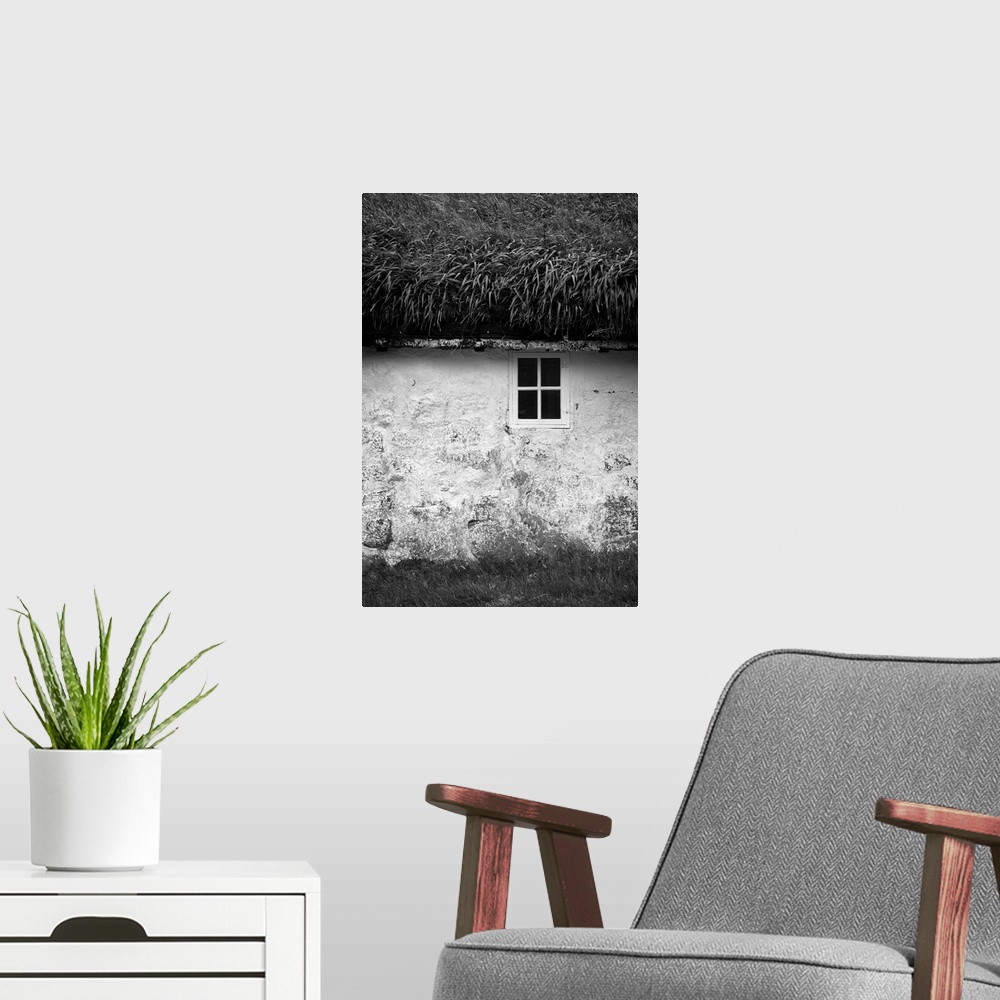 A modern room featuring Black and white image of a small window in the stone wall of a house with a grassy roof.