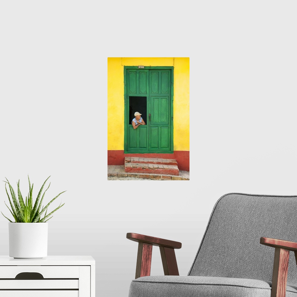 A modern room featuring Photograph of a man leaning through a window connected to a large green door on a yellow and red ...