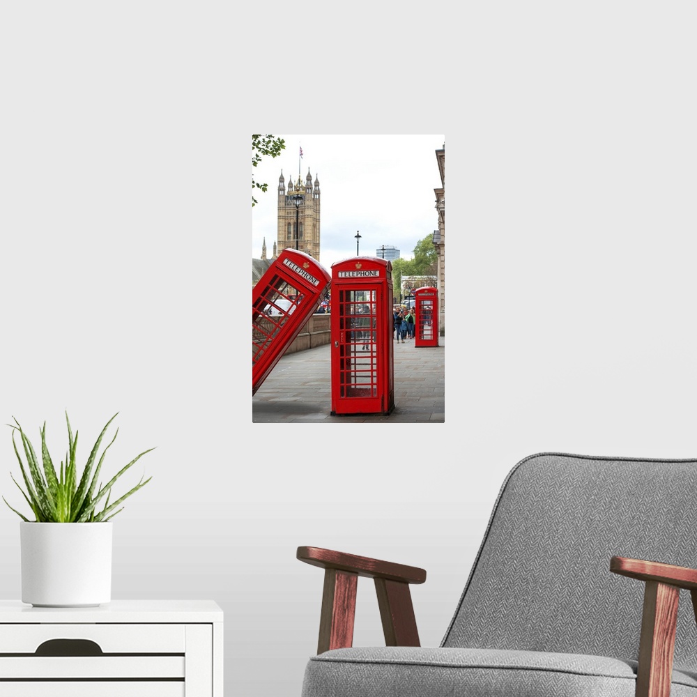 A modern room featuring Three red phone booths, one leaning against the other, with the House of Parliament in the backgr...