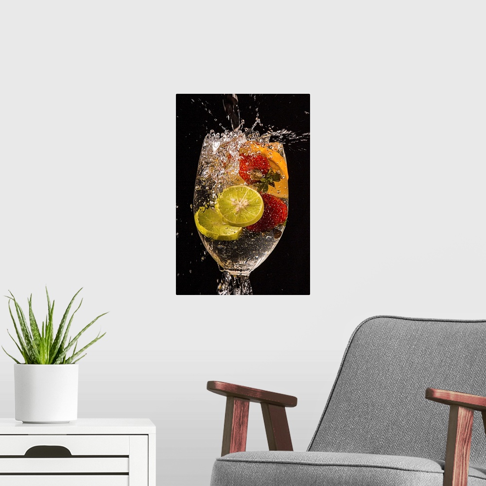 A modern room featuring Slices of lemons and oranges and whole strawberries splashing into a glass of water.