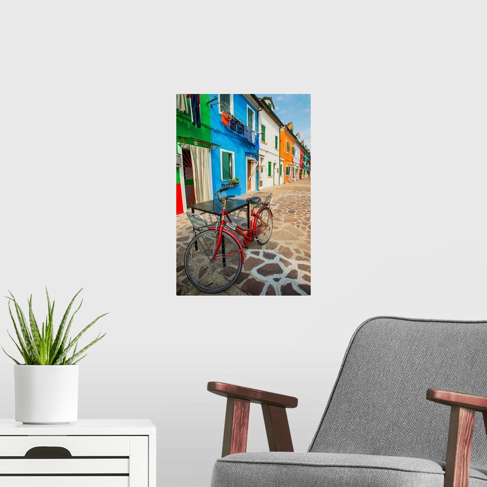 A modern room featuring Photograph of a red bicycle leaning on a table outside of a row of vibrant fishermen's homes in B...