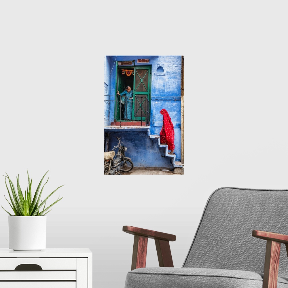 A modern room featuring Woman with red Sari walking up steps in the blue city of Jodphur, India.