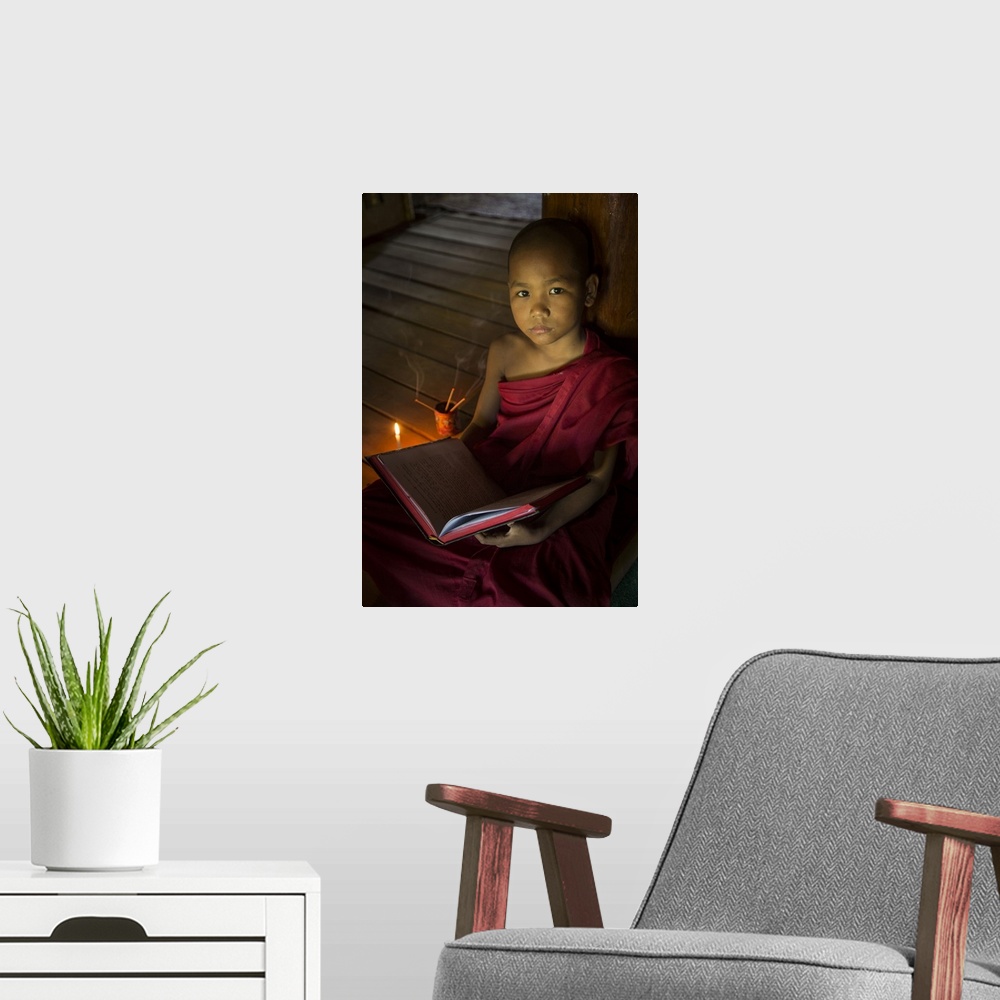 A modern room featuring Young Burmese monk reading by candlelight