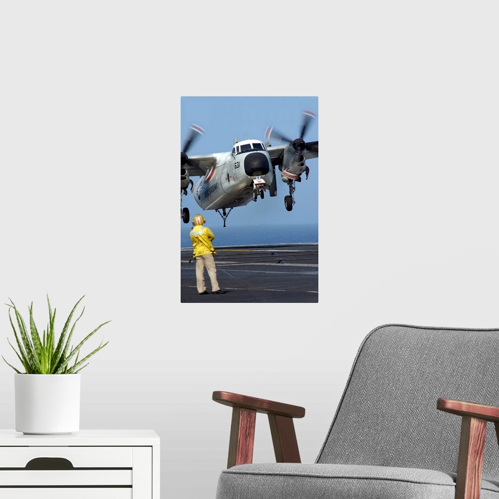 A modern room featuring A US Navy officer observes a C2A Greyhound aircraft landing onboard USS Harry S Truman