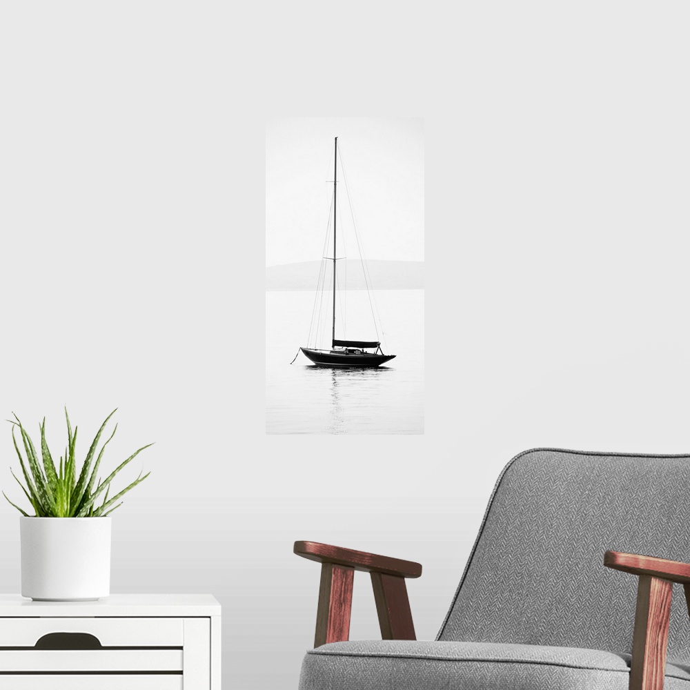 A modern room featuring Black and white photograph of a sailboat with its sail down on calm water.