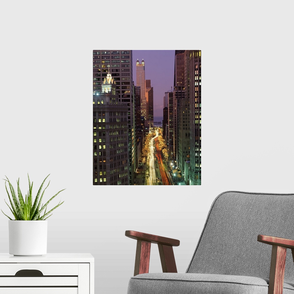 A modern room featuring A vertical picture taken in between skyscrapers that line a street in Chicago with cars lights st...