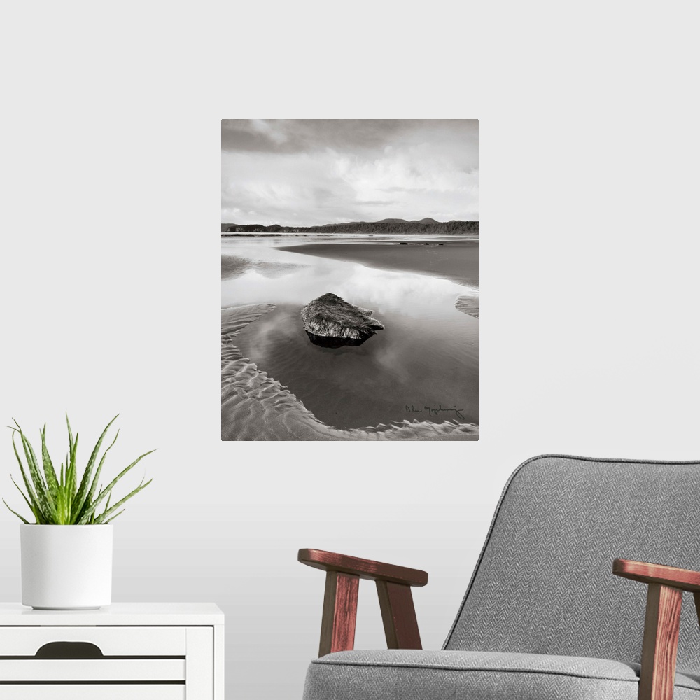 A modern room featuring A black and white photograph of an idyllic beach scene, with a large rock in the foreground.