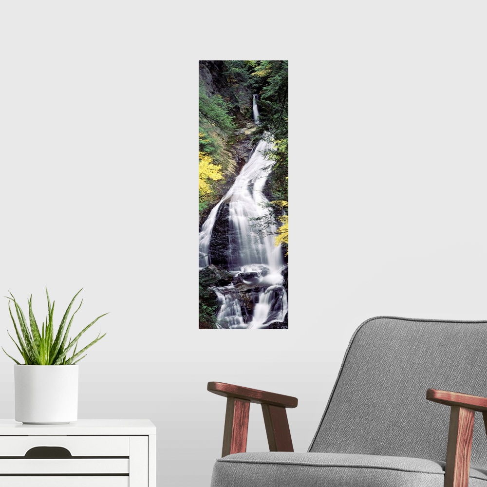 A modern room featuring Vertical, large photograph of Moss Glen Falls surrounded by rocky terrain and fall foliage, in th...