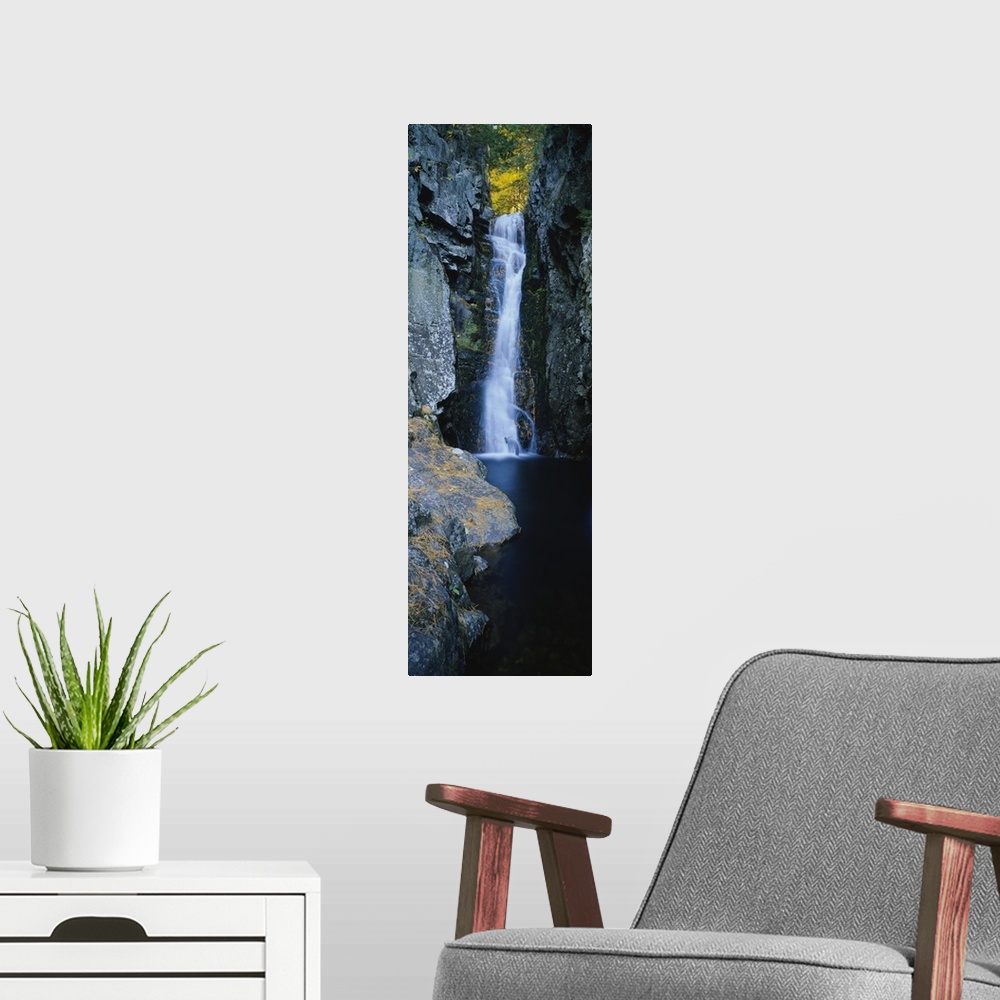 A modern room featuring Vertical photograph on a giant canvas of a large waterfall surrounded by the rocky edges of a for...