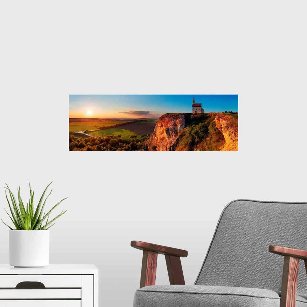 A modern room featuring Panoramic image of a church on a cliff overlooking a village in Slovakia at sunset.