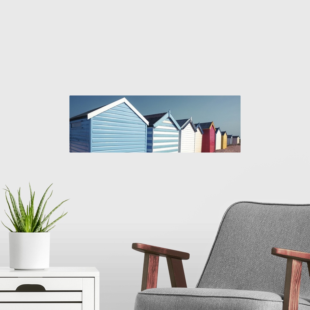 A modern room featuring A panoramic image of a long line of colorful beach huts on a clear day.