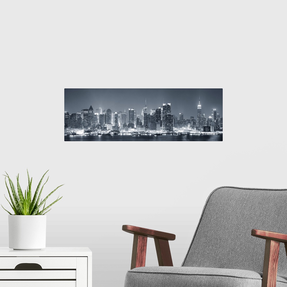 A modern room featuring Manhattan midtown skyline in black and white at night with skyscrapers lit over Hudson River with...
