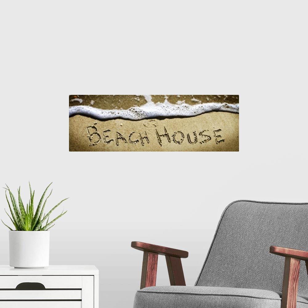 A modern room featuring The word "Beach House" drawn in the sand near the ocean water.