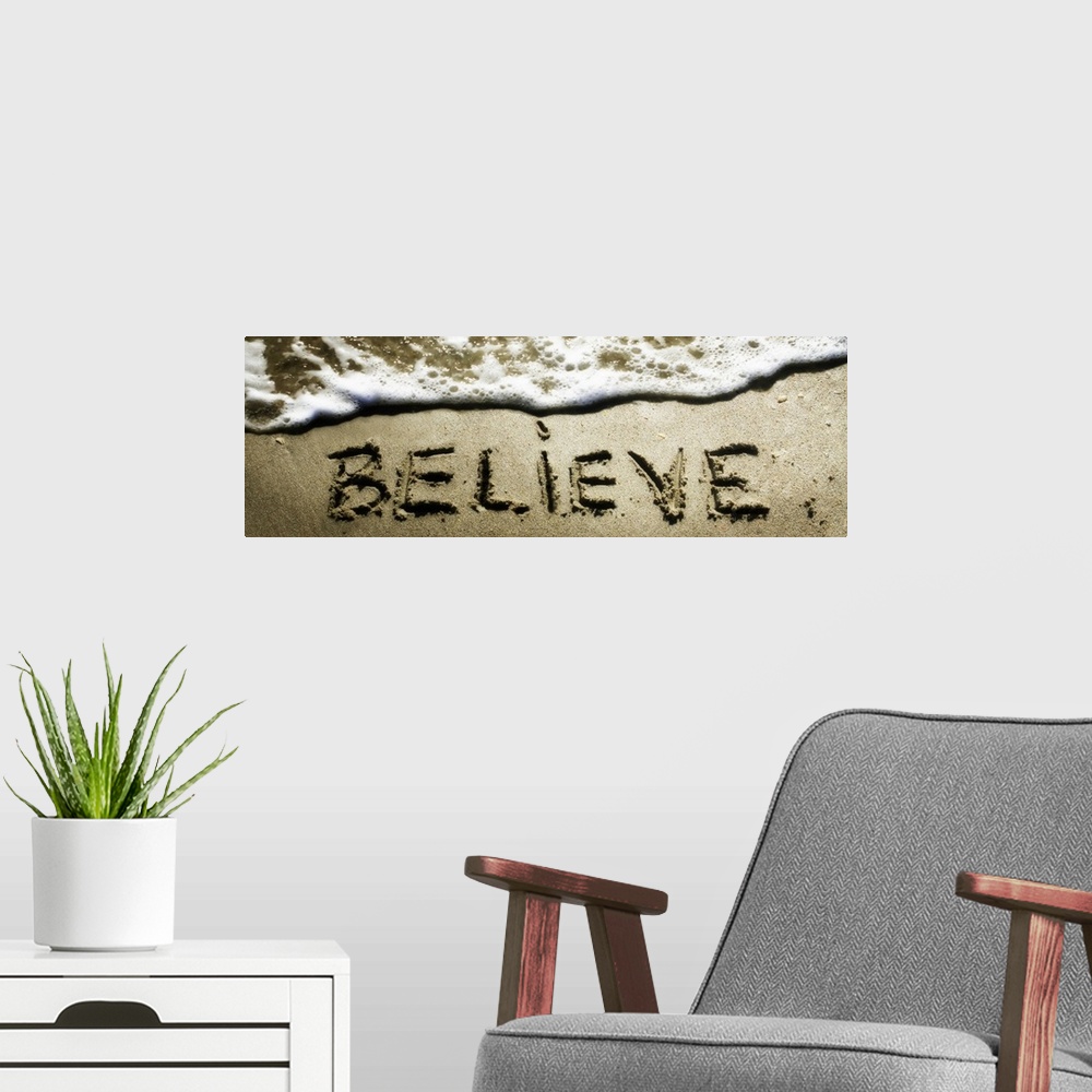A modern room featuring The word "Believe" drawn in the sand near the ocean water.