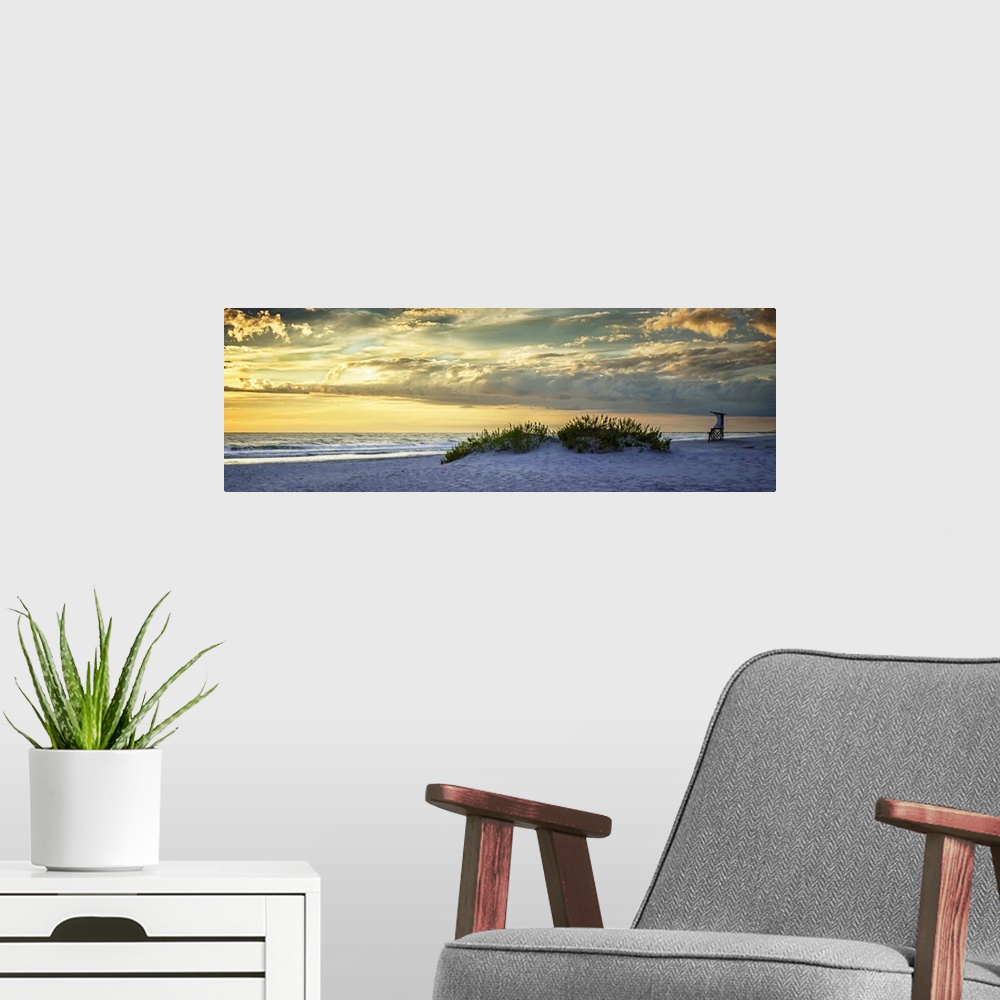 A modern room featuring Cloudy sky at sunrise glowing yellow over the beach.