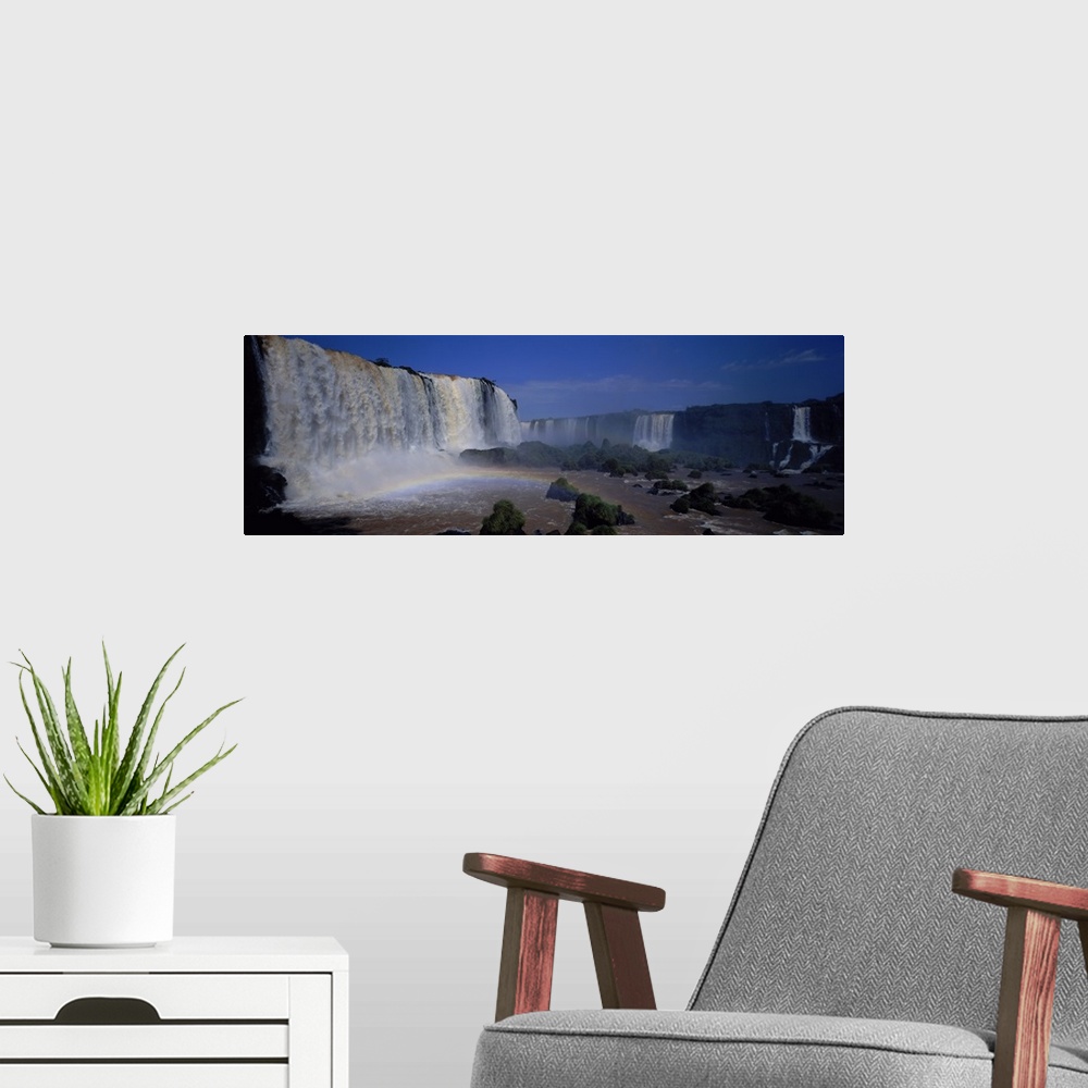A modern room featuring This is a panoramic photograph of enormous South American waterfalls and a rainbow forming under ...