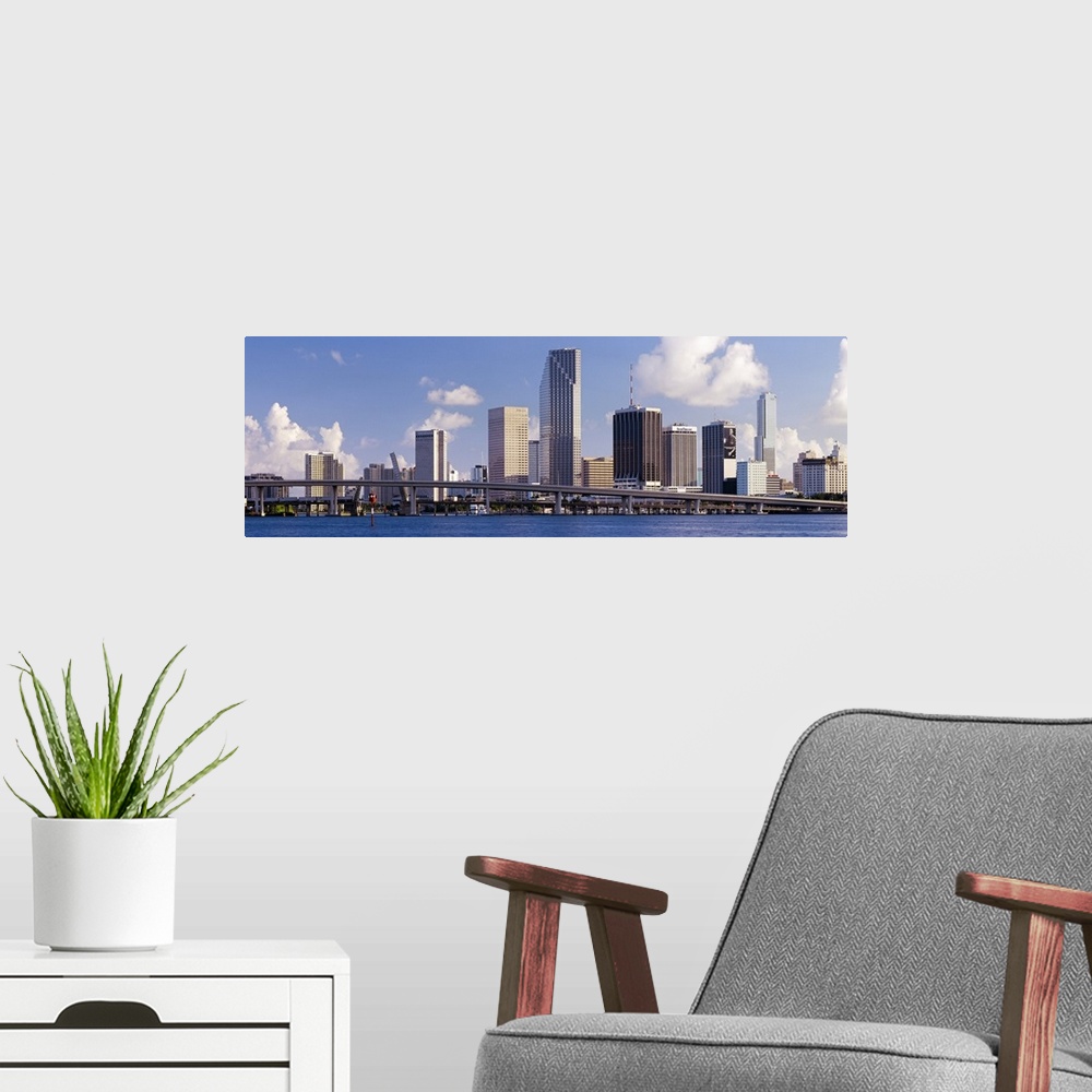 A modern room featuring This urban landscape wall art is the city skyline taken from the water with a roadway passing in ...