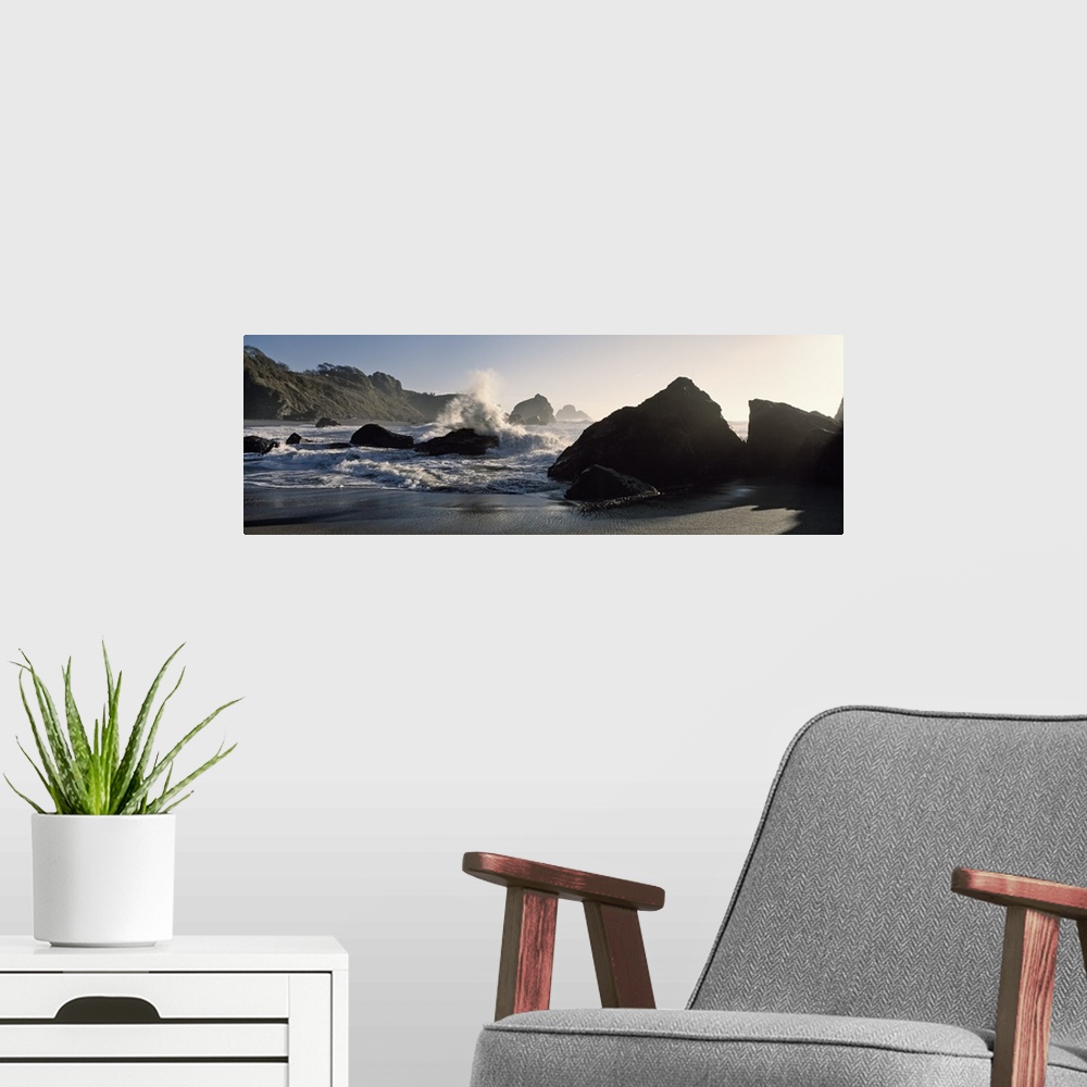 A modern room featuring Panoramic photograph of shoreline with huge boulders with ocean waves and spray.