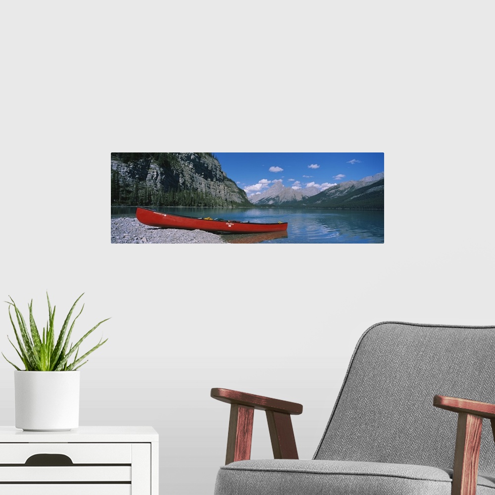 A modern room featuring A long canoe is pictured in wide angle view as it sits half in half out of the water. Mountainous...
