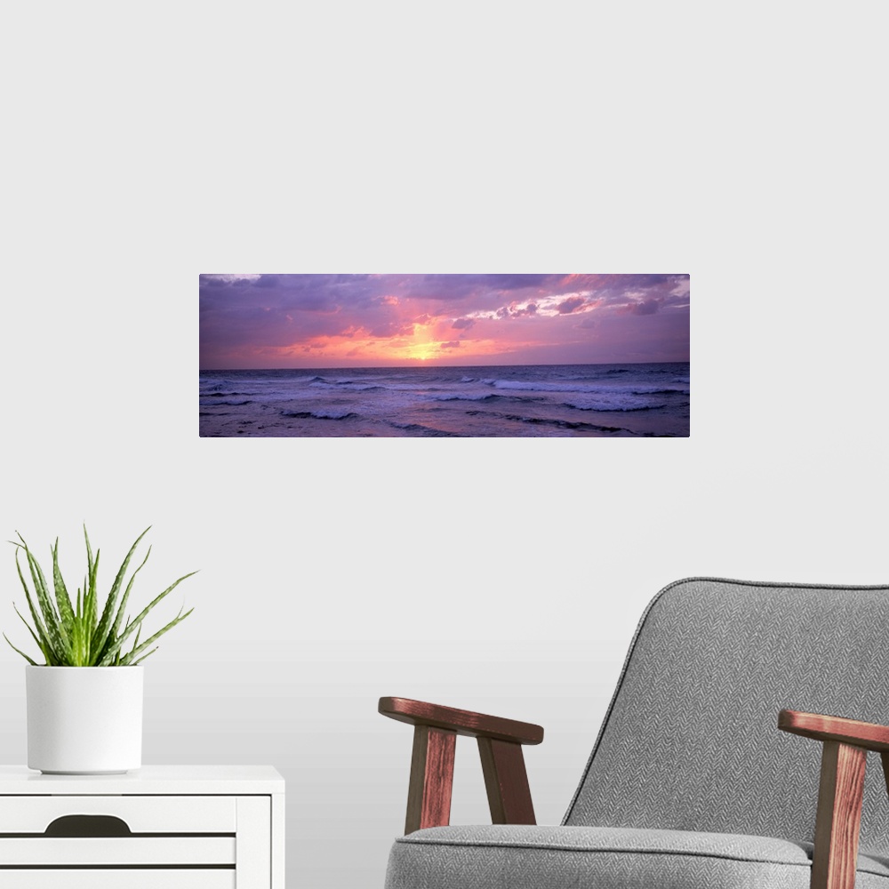 A modern room featuring Panoramic photograph shows the glow of the sun as it begins to set behind a group of clouds and s...
