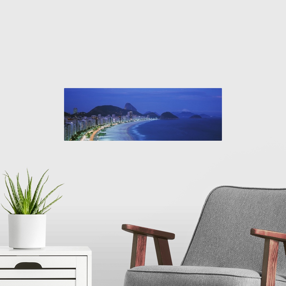 A modern room featuring A large panoramic shot of the coast and skyline of Rio De Janeiro. Taken at dusk, the buildings a...