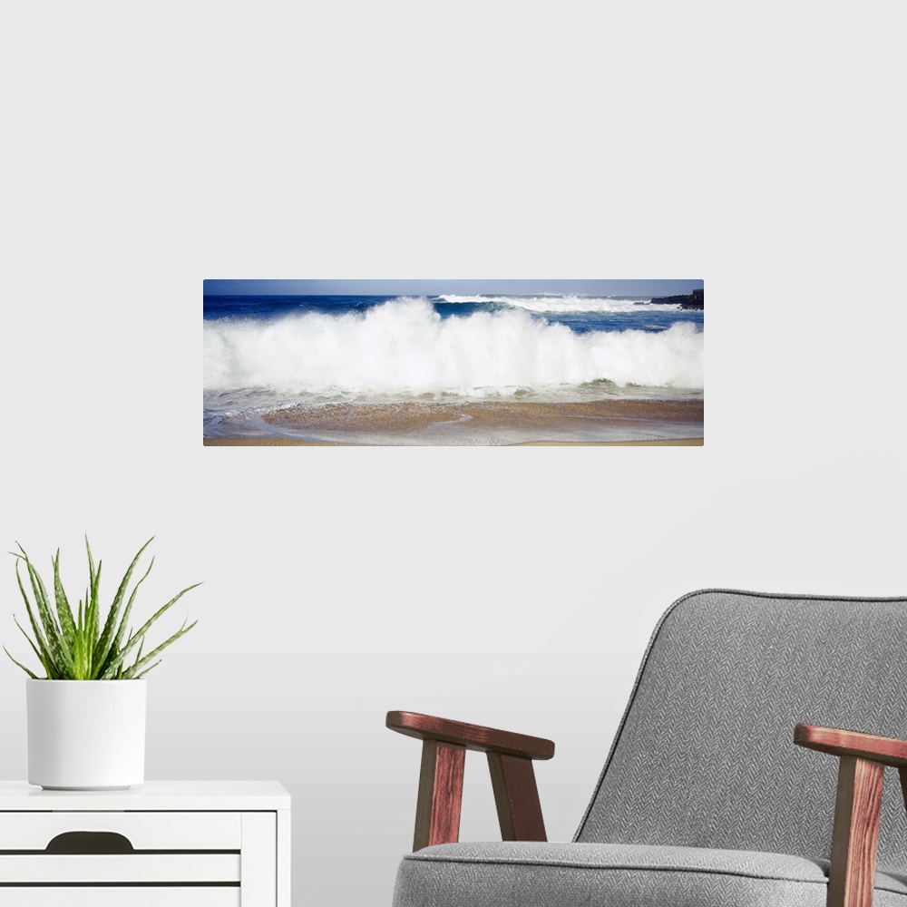 A modern room featuring Panoramic photograph of large waves crashing into the beach, bright blue water in the background,...