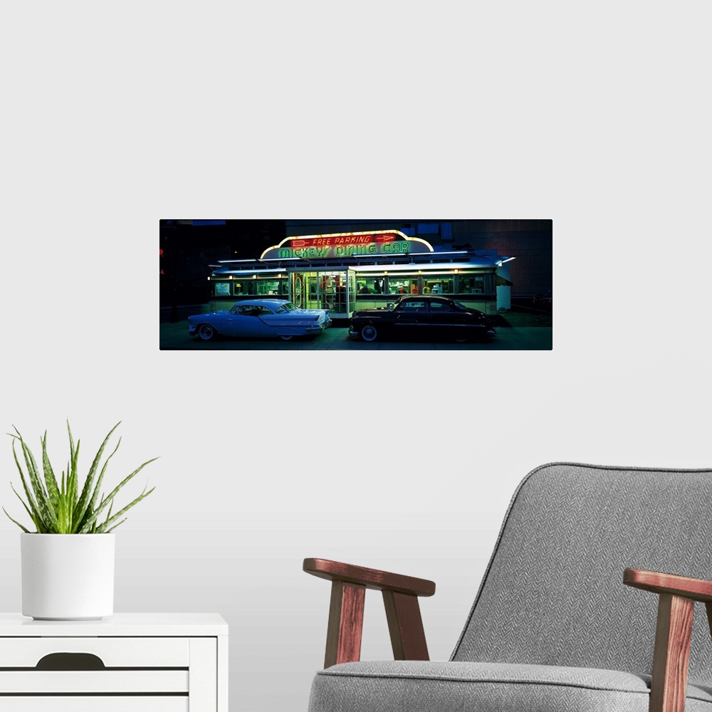 A modern room featuring Panoramic photograph of two vintage cars sitting outside of a lit up eatery at night with neon si...