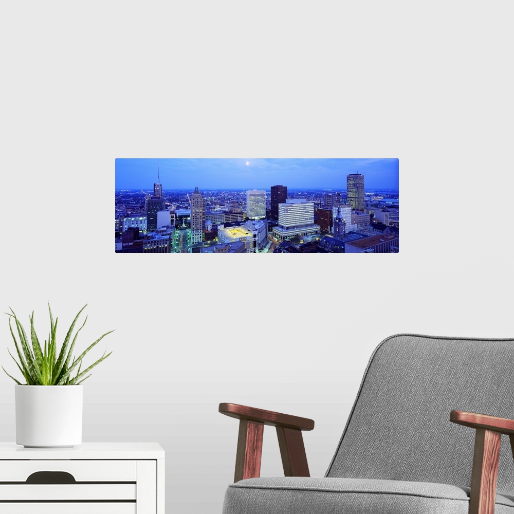 A modern room featuring This panoramic wall art is an aerial photograph of the city skyline at dusk with moon shining dow...