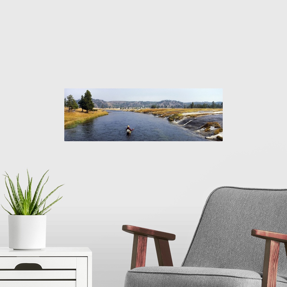 A modern room featuring Wide angle shot of a person standing in thigh high water fishing with a beautiful view of park te...