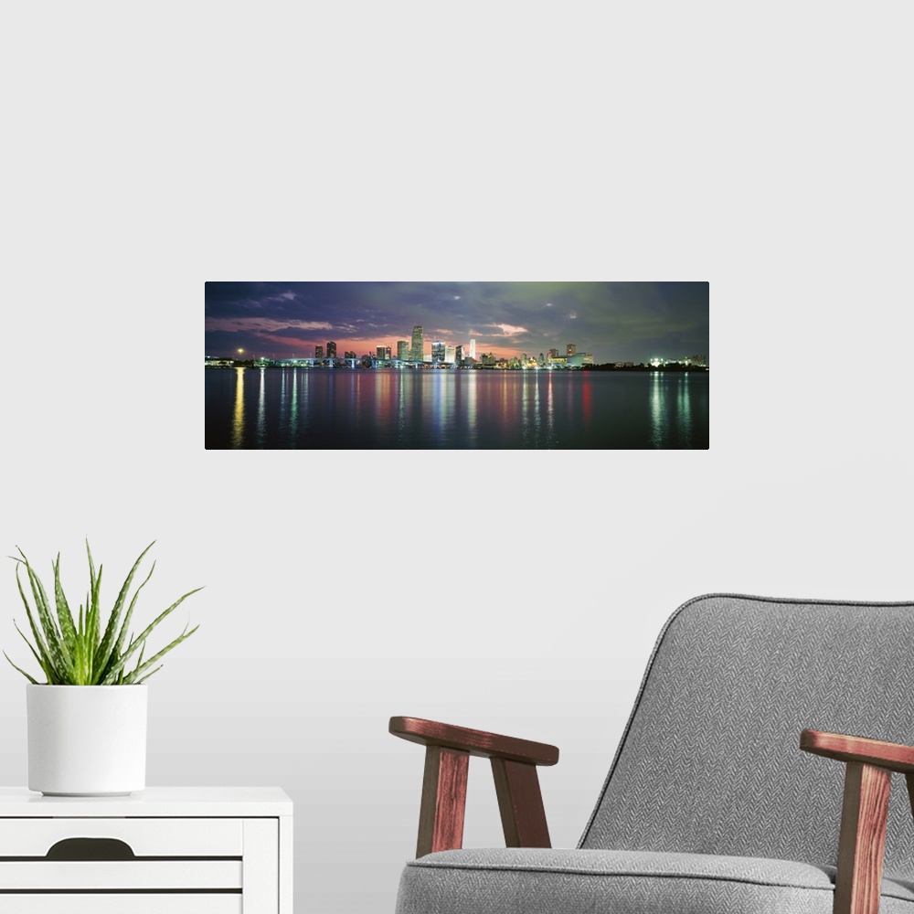 A modern room featuring This city scape photograph shows the city from a distance reflecting on the water on panoramic sh...